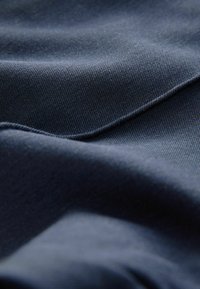 Donkerblauwe stof met een gladde textuur en subtiele glans, met diagonale weefpatronen en zachte plooien.