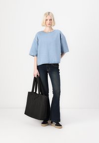 Ανοιχτού μπλε τζιν oversized μπλούζα με κοντά μανίκια, σε συνδυασμό με σκούρα καμπάνα τζιν. Μια μαύρη τσάντα tote κρέμεται από το δεξί χέρι, με ανθεκτικές λωρίδες.