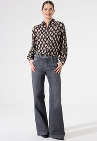 Blouse à manches longues, à motif noir et beige, associée à un jean évasé gris taille haute. Le tissu semble léger et lisse.