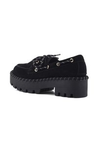 Scarpe platform in suede nero con suola in gomma spessa, dotate di occhielli dorati e lacci bianchi e neri. Punta arrotondata e suola testurizzata.