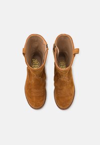 Ein Paar braune Wildleder-Stiefeletten mit Zuglaschen und sichtbaren Nähten, von oben auf einem weißen Hintergrund betrachtet.