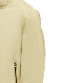 Beige Außenjacke mit glatter Textur, schrägen Nahtdetails und einer Reißverschlusstasche auf der linken Seite.