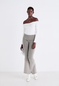 Off-the-shoulder vit topp som kombineras med högmidjade, texturerade grå trikåbyxor med randigt mönster och knappribbor längs sidorna.