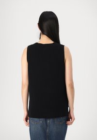 Svart ermeløs strikket topp med rund hals, løs passform og splitt i sidene; kombinert med høyt liv blå denim jeans.