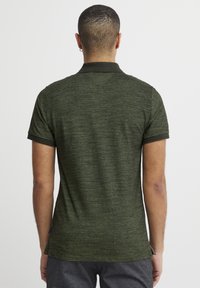 Kortærmet polo t-shirt i mørkegrøn, struktureret stof med kontrasterende sort krave og ærmekant. Har sideslids i kanten.