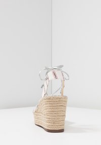 Białe sandały na koturnie z espadryli z plecionym obcasem z juty, srebrnymi akcentami oraz wstążkowymi sznurówkami z detalami logo na paskach.
