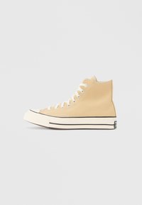 Μπεζ ψηλό πάνινο παπούτσι με λευκά κορδόνια, καουτσούκ μύτη και μαύρη λεπτομέρεια κατά μήκος της σόλας· ελάχιστο λογότυπο στη φτέρνα.