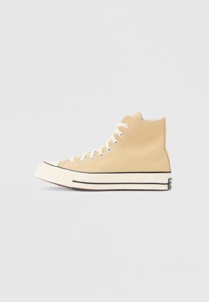 Sneaker alta in tela beige con lacci bianchi, punta in gomma e bordo nero lungo la suola; marchio minimal sulla parte posteriore.