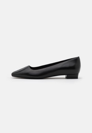 Chaussure plate en cuir noir avec un bout pointu, un talon bas superposé et une texture lisse, présentant un design sans coutures et des détails minimaux.
