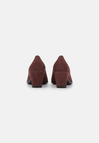 Scarpe con tacco alto in suede bordeaux scuro, con punta arrotondata e un tacco a blocco modesto. Tessuto liscio con sottili dettagli di cucitura sul retro.