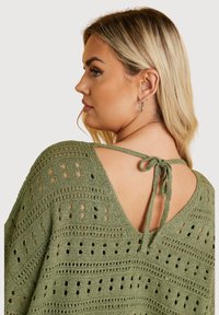 Olivgrön stickad topp med öppen rygg och knytning, intrikat perforerat mönster och en avslappnad passform.