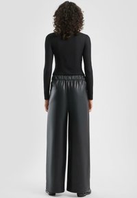 Czarna bluzka z długim rękawem o prążkowanej fakturze zestawiona z czarnymi, szerokimi spodnimi z imitacji skóry, wyposażonymi w elastyczną talię i gładką powierzchnię.