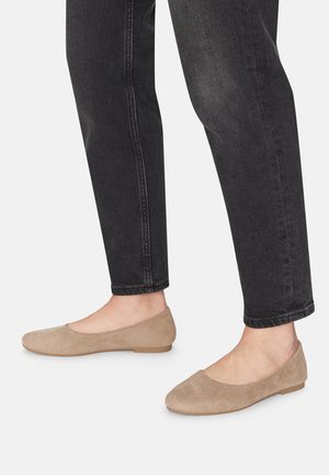 Beige Wildleder Ballerinas mit runder Spitze und flexibler, flacher Sohle, kombiniert mit schwarzen Jeans, die ein schlankes und minimalistisches Design zeigen.
