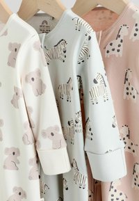 Tre babybeklædninger på træhangere: cremefarvet med koala-print, lysegrøn med zebra-print, og lyserød med giraffe-print. Blød bomuldsstruktur.