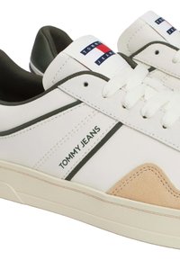 Zapatillas de cuero blancas con acentos verdes y detalles de ante beige. Presentan un logo en la lengüeta y suela de goma texturizada. Diseño clásico de caña baja.