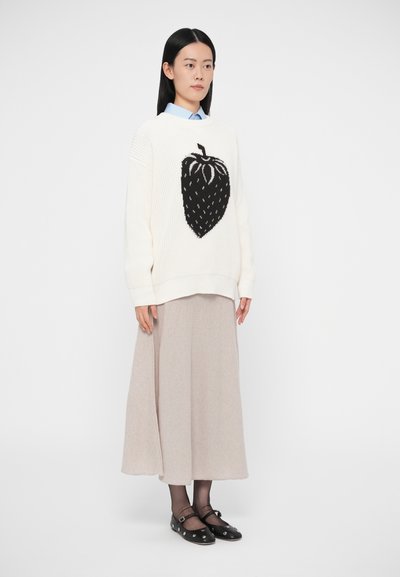 Camisola de malha creme com um desenho preto de morango, combinada com uma saia longa bege e sapatos pretos com detalhes em prata.