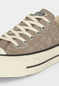 Μπεζ Converse χαμηλού τύπου αθλητικό παπούτσι με εκρού κορδόνια, ύφασμα με σχέδιο πεϊσλί, μεταλλικές θηλιές και παχύ, εκρού χρώματος καουτσούκ με μαύρη ρίγα.