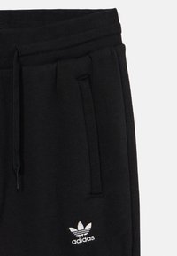 Pantalons de survêtement noirs avec une taille élastique et un cordon de serrage, dotés de poches latérales et d'un logo Adidas blanc sur la cuisse gauche.