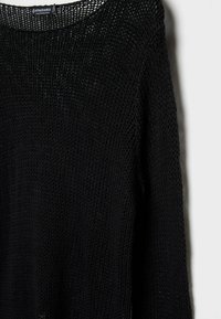 Pull tricot noir avec une texture lâche et épaisse, encolure large et manches longues. Motif à mailles ouvertes distinct tout au long du tissu.