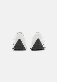 Baskets de sport blanches avec un dessus texturé, présentant des accents noirs et une semelle noire texturée en forme de triangle. La vue arrière met en valeur les détails de conception.