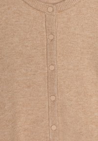 Lys beige cardigan laget av myk strikket materiale, med ribbestrikket rund hals og seks matchende knapper foran.