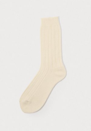 Calzino beige a coste con una texture liscia, caratterizzato da una punta rinforzata e una comoda cuffia elastica.