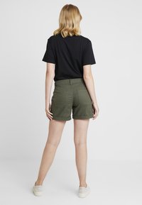 Back view of a person wearing a black t-shirt and olive green shorts. The shorts feature rolled hems and two back pockets.