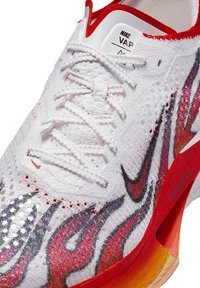 Scarpa Nike Vapor con tomaia bianca testurizzata decorata da motivi a fiamma rossa e grigia, con lacci bianchi e suola trasparente arancione.