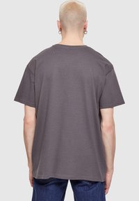 Over-sized grå T-shirt med ribbet tekstur, korte ærmer og en klassisk rund halsudskæring, parret med mørkeblå jeans.