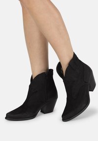 Botines de ante negros con punteras puntiagudas, tacones de bloque de altura media, cremalleras laterales y costura decorativa a lo largo de la parte superior.