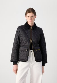 Zwart gewatteerd jack met een zachte kraag, gouden rits en hardware, twee voorzakken en geribbelde manchetten. Heeft een getailleerde pasvorm.