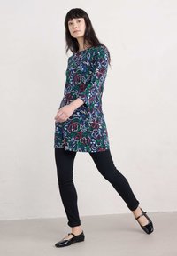 Blusentunika mit floralem Muster in Marineblau und roten, grünen sowie blauen Akzenten. Lange Ärmel, gerade geschnitten, kombiniert mit schwarzen Slim Jeans und schwarzen Ballerinas.