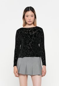 Schwarz gemusterte Bluse mit langen Ärmeln aus strukturiertem Stoff, rundem Ausschnitt und geradem Saum, kombiniert mit einem grauen, plissierten Rock.