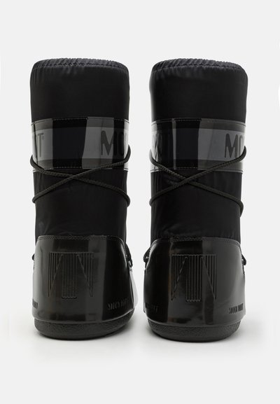 Bottes noires isolées avec une finition brillante, un haut élastiqué et une bande transparente contrastante avec un logo en relief. Semelle texturée.
