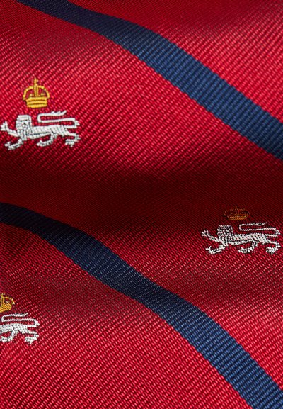 Tissu à rayures rouges avec une bande diagonale bleu marine et des motifs brodés de lion et de couronne en blanc et or. Surface texturée.