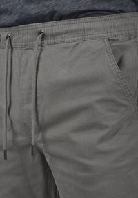 Lightweight, grey cotton jogging pants with an elastic waistband, drawstrings, and side pockets; smooth texture with a relaxed fit.