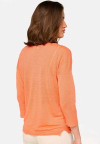 Pull léger orange en maille avec des manches ¾, des poignets côtelés et une coupe décontractée, présentant un ourlet arrière légèrement plus long.