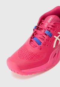 Baskets de sport roses vives avec une tige texturée, des lacets bleus et un logo blanc. Présente un bout arrondi et une semelle rembourrée et flexible.