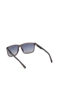 Gafas de sol con un marco transparente gris oscuro, lentes degradados azules y patillas negras con un diseño estampado. Diseño simple de forma rectangular.