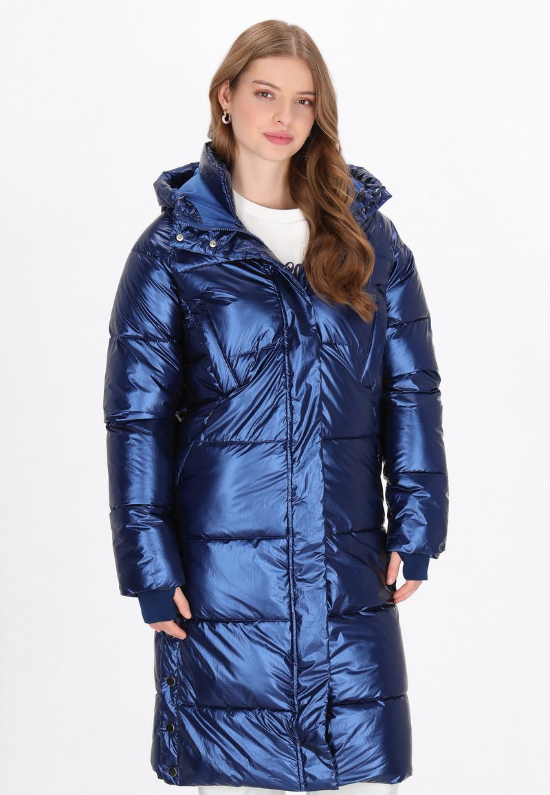 Hosszú kék puffertakaró, fényes anyagból készült, kapucnival, cipzárral elöl és bordás mandzsettákkal. Kiemelkedő a steppelt, párnázott kialakítása.