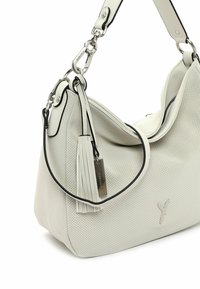 Sac à main en cuir perforé blanc avec un design doux et décontracté. Présente un bord noir, des accessoires en argent et un pompon décoratif avec une étiquette.