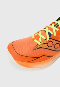 Chaussure de sport orange avec une tige en mesh respirant, des lacets jaunes vifs, des accents noirs subtils et une semelle texturée pour l'adhérence.