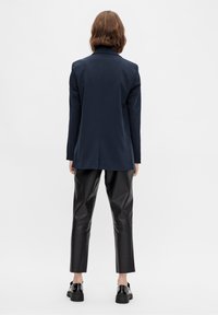 Marinblå blazer med en kroppsnära silhuett och slagkragar, parat med blanka svarta lädercroppade byxor och svarta snörskor.