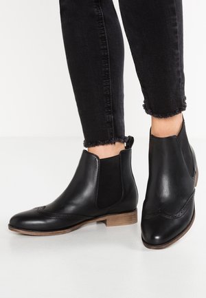 Botas de tobillo de cuero negro con punta redonda, paneles laterales elásticos y detalles de perforación. Tacón en bloque de aspecto madera y suela texturizada.