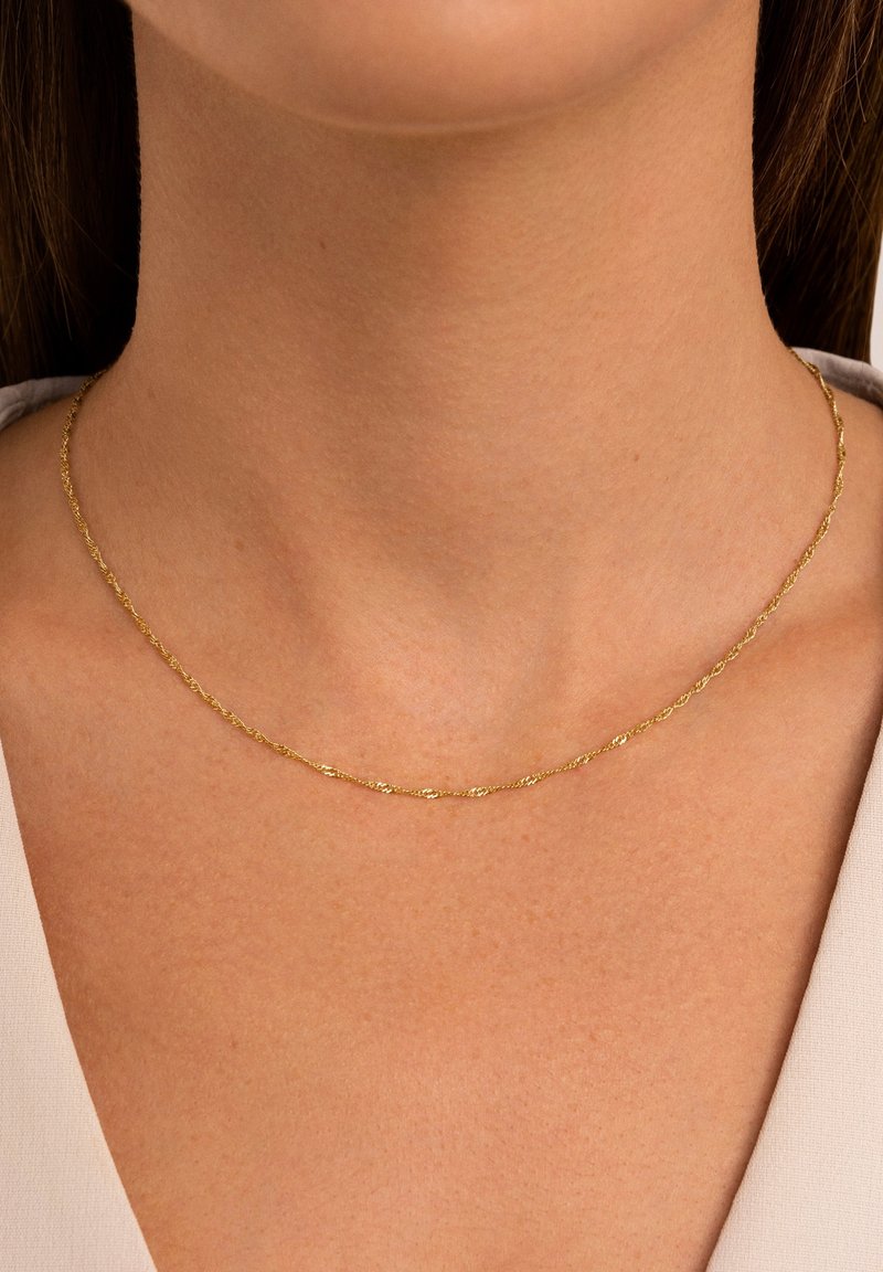 Gouden gedraaide ketting die op een gladde nek rust, met een delicate textuur en een ingetogen ontwerp, geschikt om te layering.