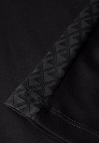 Musta kangas sileällä pinnalla, jossa on kuviollinen musta reunus. Reunuksessa on geometrinen muotoilu reunalla.