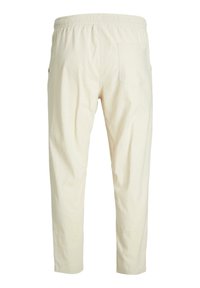 Light beige trousers with an elastic waistband, tapered legs, and one rear patch pocket for added detail. Soft, textured fabric.