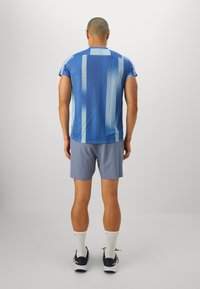 Blue patterned athletic shirt with short sleeves, paired with light gray shorts. The shirt features vertical stripes and a textured design.