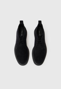 Botines de ante negro con textura suave, punta redonda y cierre con cordones. Diseño minimalista con una pestaña en la parte posterior.