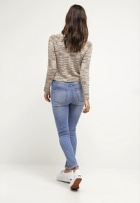 Jeans skinny azzurri con vita alta, abbinati a un maglione beige texturizzato e sneakers bianche, visti da dietro.